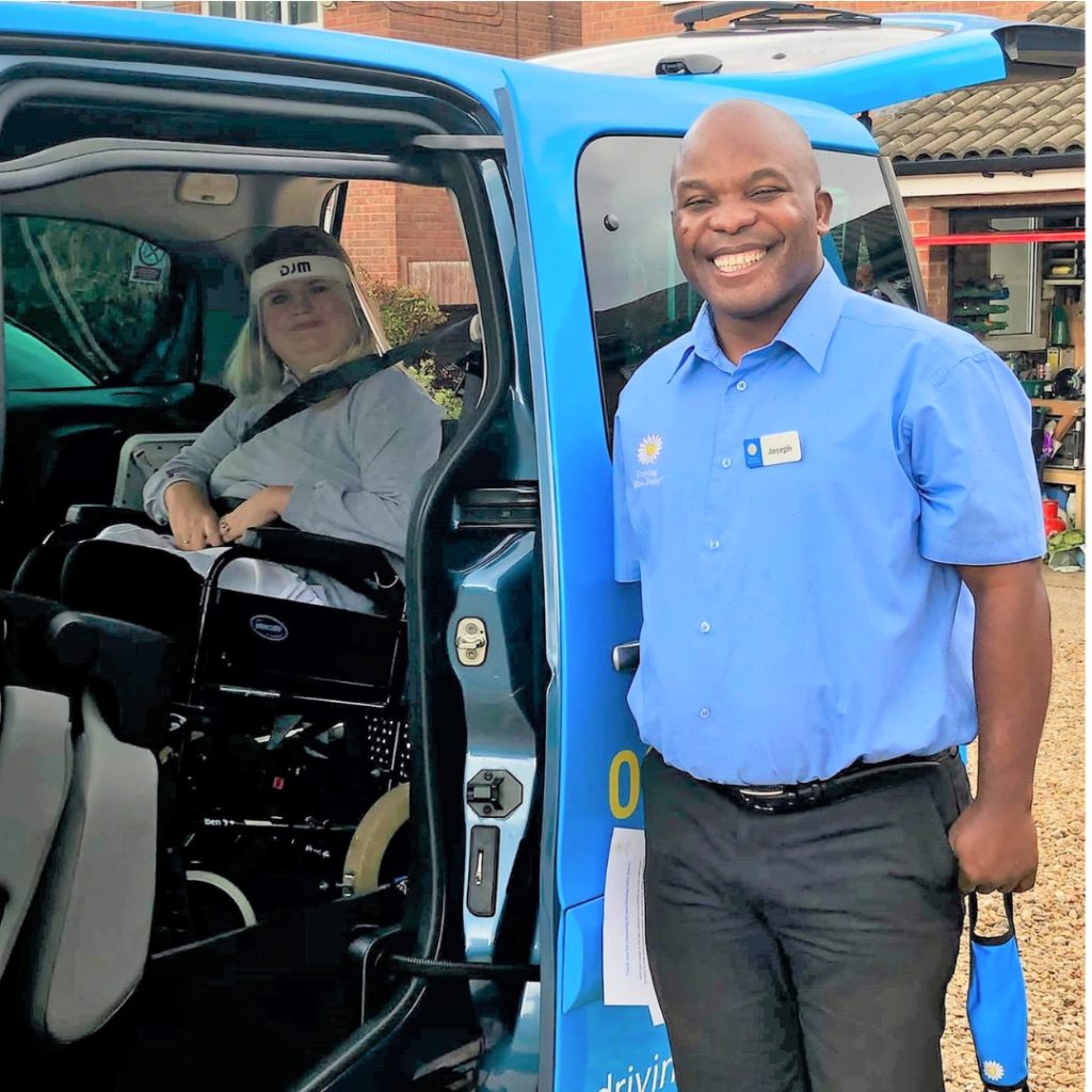 A Patient Transport in Driving Miss Daisy unifrom standing next to a wheelchair accessible vehicle with a client in the back.
