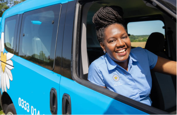 Driving Miss Daisy business owner smiling from the window of her blue vehicle