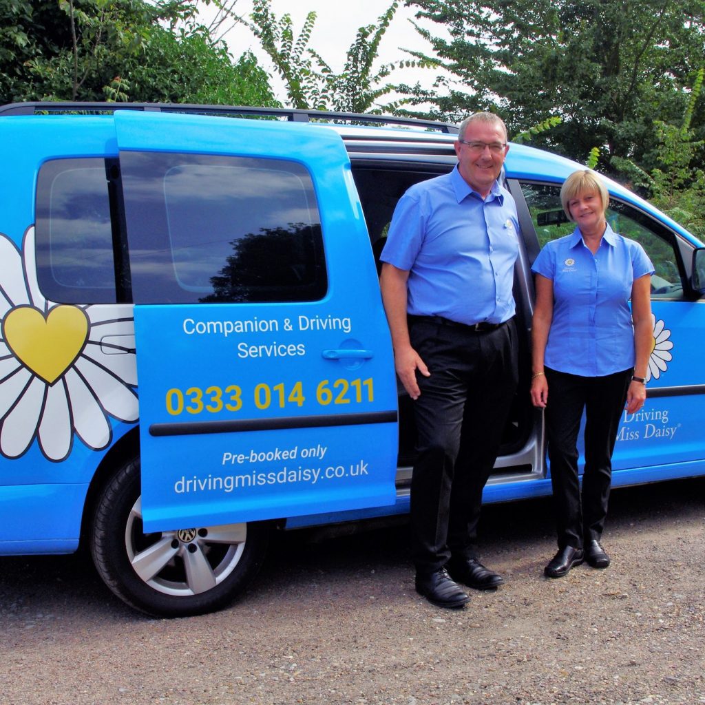 Two companion drivers wearing driving miss daisy uniform standing next to a wheelchair accessible vehicle