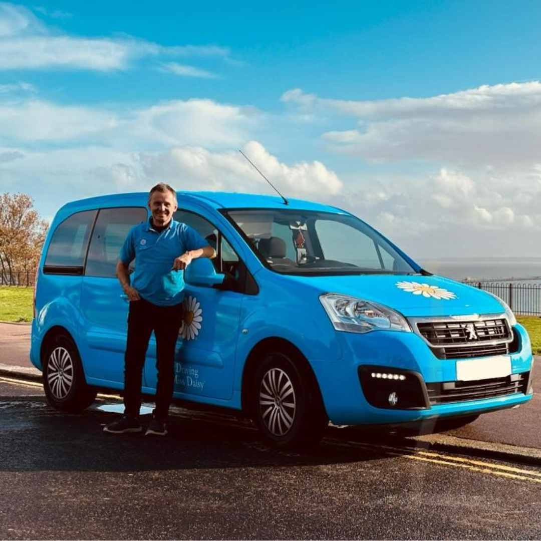 a companion driver in driving miss daisy uniform standing next to a wheelchair accessible vehicle.