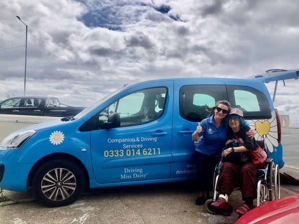 A Companion driver standing with a client in front of a driving miss daisy wheelchair accessible vehicle