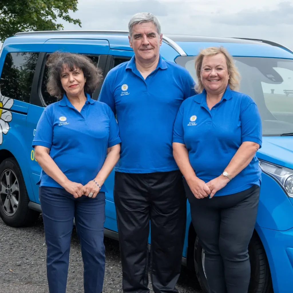 Three companion drivers in Driving Miss Daisy uniform standing in front of a Driving Miss Daisy wheelchair accessible vehicle.